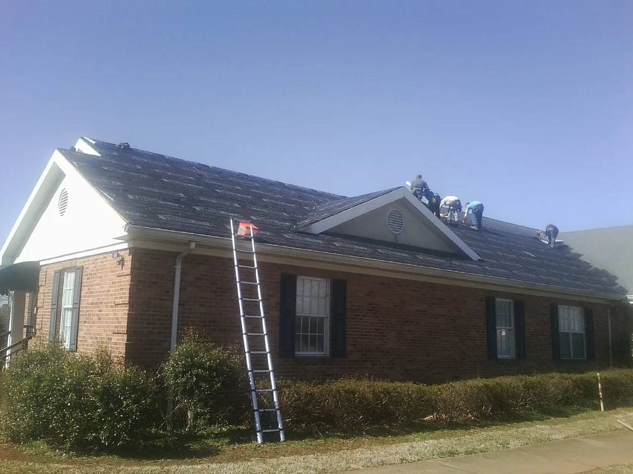 Crew tearing shingles off a brick ranch roof with a ladder set — Emergency Roof Repair work by our crew in Parker